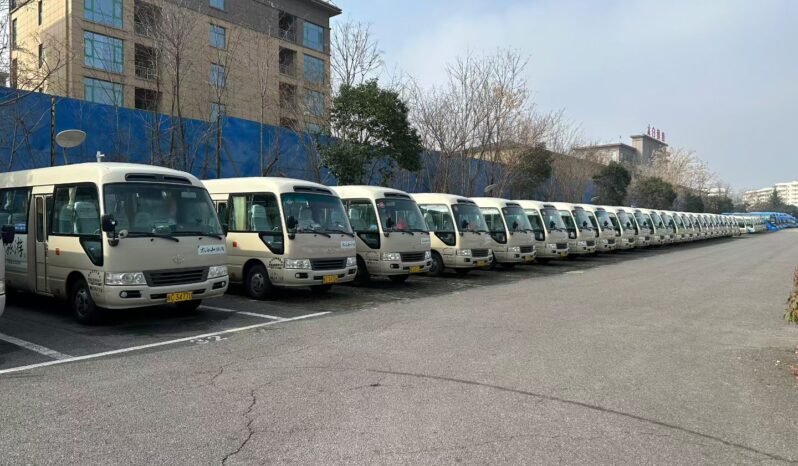 Front view of three beige used Toyota Coaster minibuses parked in a row. These units are from a premium Chinese tourism fleet, featuring original Toyota logos and clean, well-maintained exteriors. The photo highlights the ready-for-export condition of these 23-30 seater passenger buses in our Shenzhen inventory.