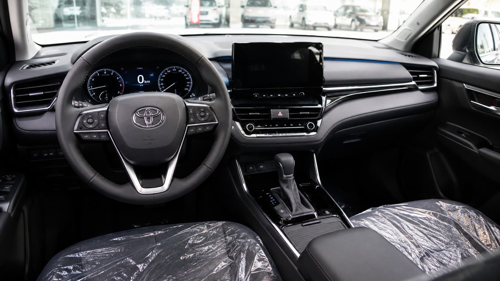 Close-up of a new vehicle interior showing the dashboard with a 0 km odometer reading, a modern center console, and plastic protective covers on the front seats, highlighting the value of a brand-new car.
