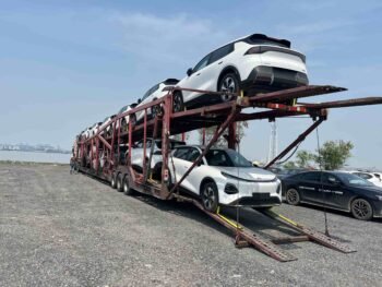 White electric SUVs loaded on a multi-level car carrier near a port area, showing vehicle transport and preparation for export shipment before international delivery.