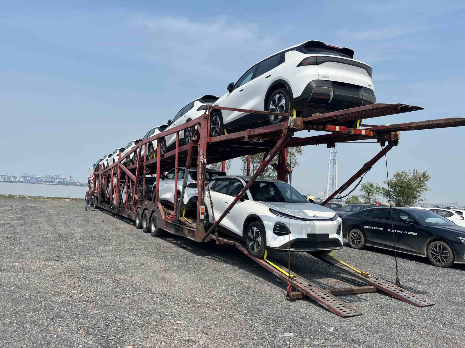 White electric SUVs loaded on a multi-level car carrier near a port area, showing vehicle transport and preparation for export shipment before international delivery.