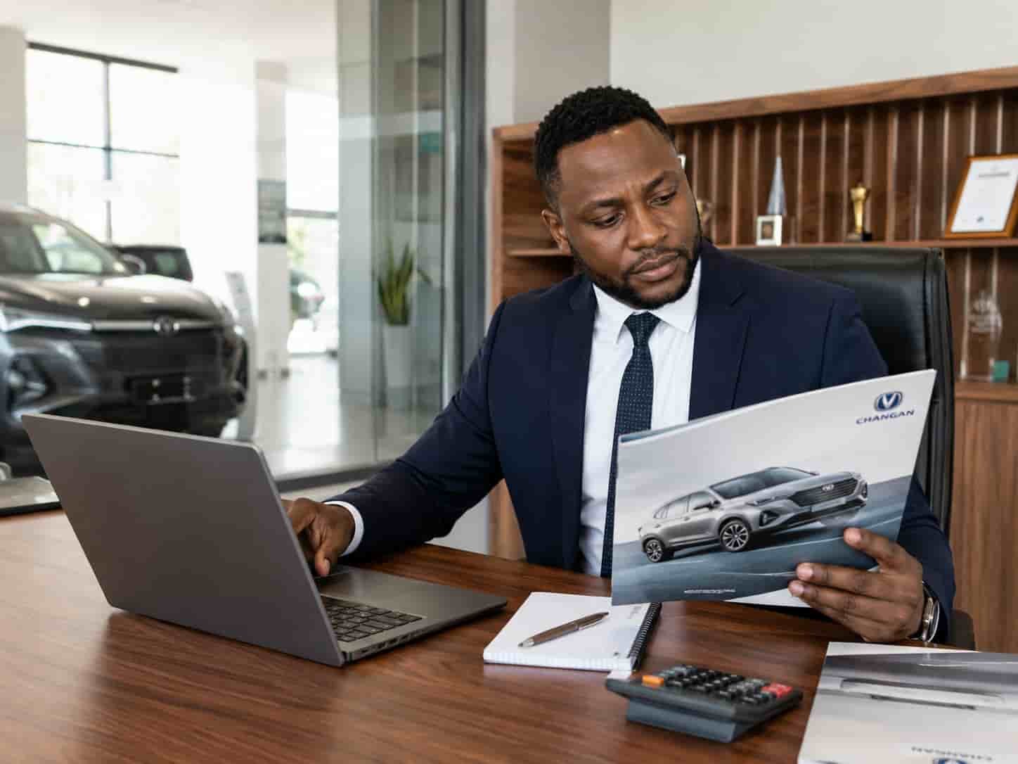 African car dealer at a desk reviewing Changan SUV specifications and FOB pricing from a Chinese vehicle exporter