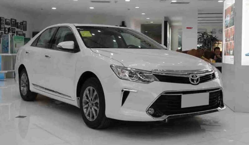 Front three-quarter view of white Toyota Camry sedan showing Toyota grille, headlights, front bumper, alloy wheels and showroom interior