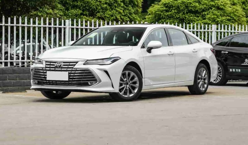 Front three-quarter view of Toyota Avalon white sedan showing Toyota grille, LED headlights, alloy wheels, side profile and outdoor vehicle display