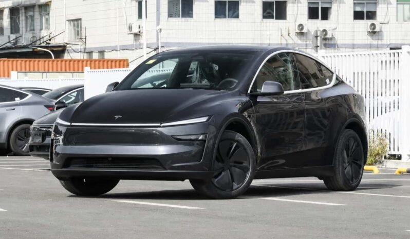 Front three-quarter view of Tesla Model Y 2026 rear-wheel drive black electric SUV showing updated front design, slim LED headlights, black wheels and parking lot exterior